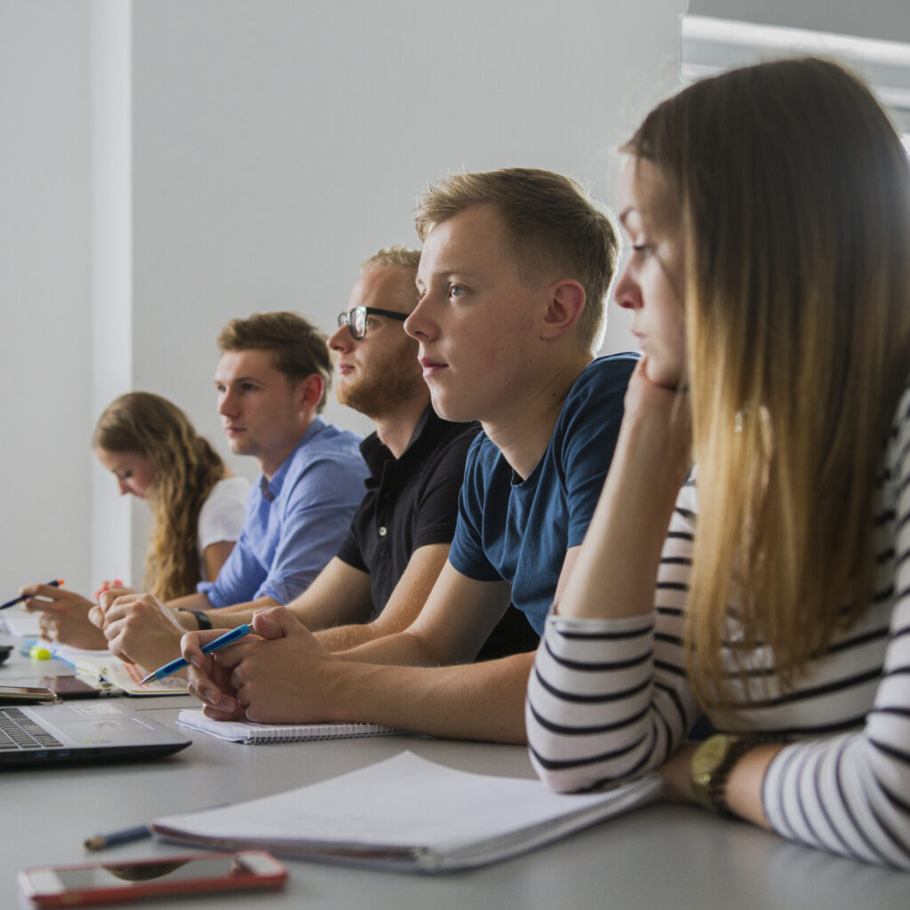 Fünf Studenten sitzen in einem Hörsaal und schauen zu dem Dozenten.